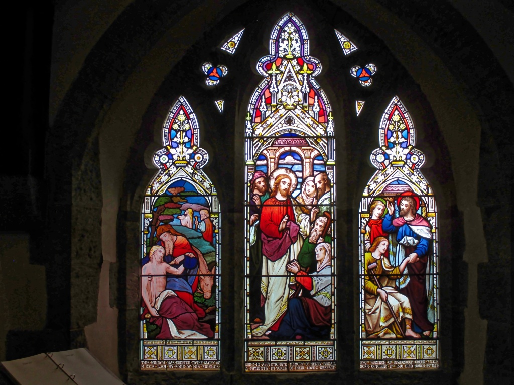 Stain glass representing The Good Samaritan, The healing of the woman with bleeding issues et Peter and John healing a Crippled Man at the Beautiful Door, St Peter ad Vincula Church, Wisborough Green, GBR, photo by Antiquary, 2018, CC BY 4.0, via Wikimedia Commons. Source : https://commons.wikimedia.org/wiki/File:First_south_aisle_window,_Wisborough_Green.jpg